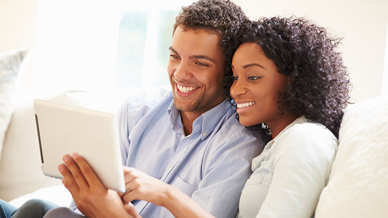 Couple seated on couch looking at iPad