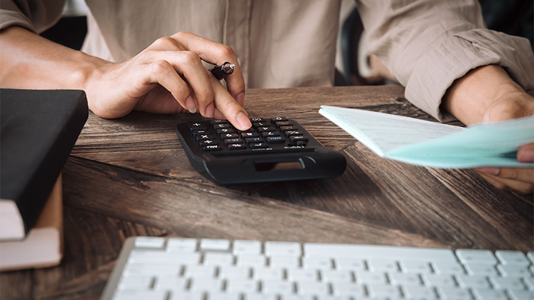 Woman at desk putting numbers in calculator while holding papers.