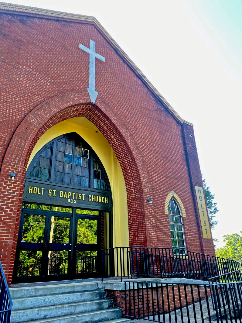 A large brick building with a cross on the façade. Words on the entrance say "Holt St. Baptist Church"