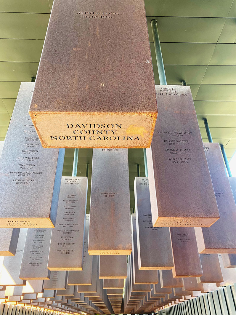 Steel rectangles hanging from ceiling with names and locations engraved on them.