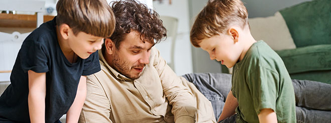 Father with sons reading book, spending time together at home and lying on the floor