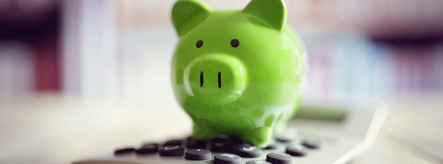Green piggy bank sitting on top of a calculator.