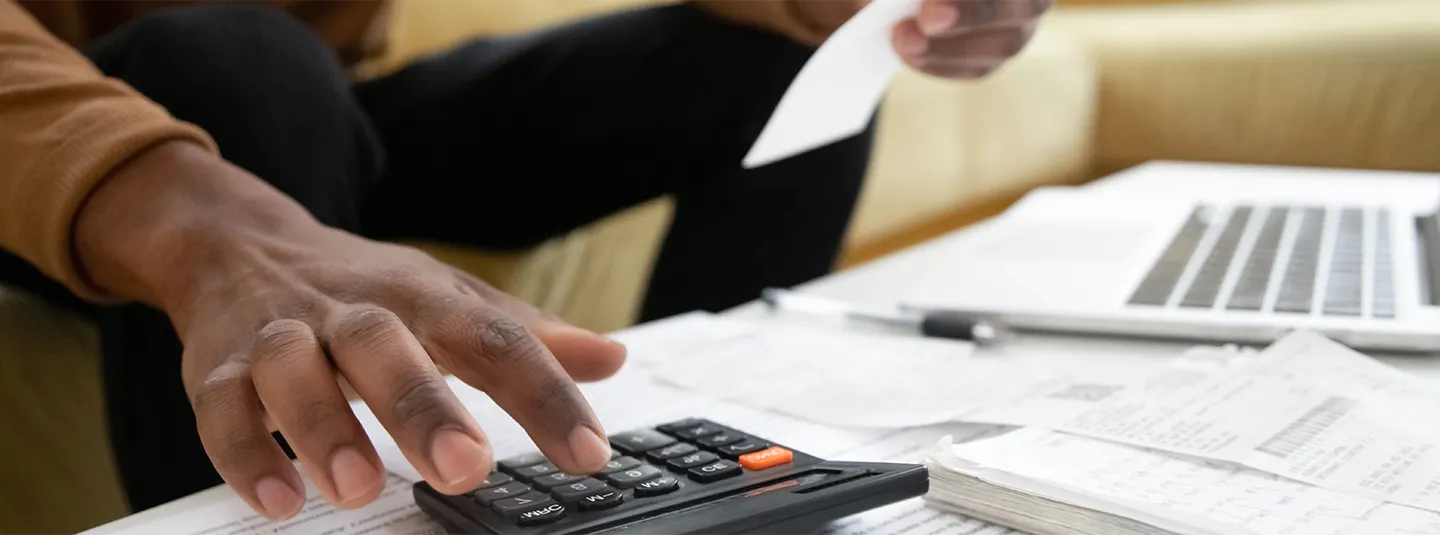 Man sitting on a couch using a calculator to calculate his taxes. 