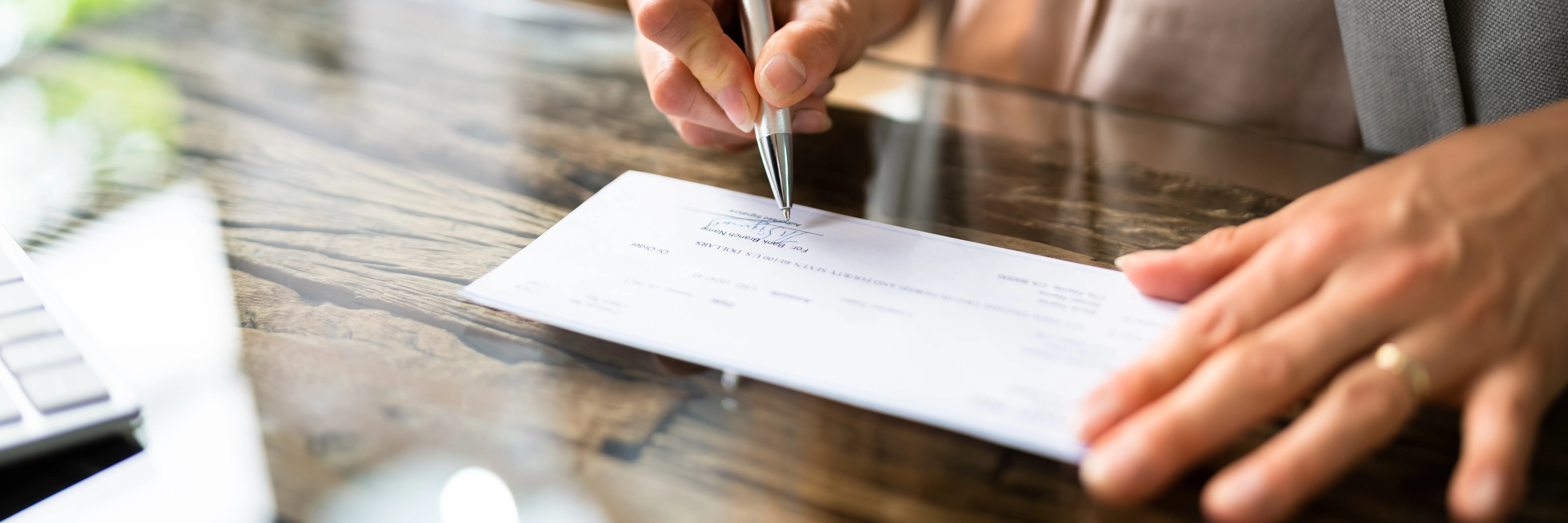 A person signing a check on a wooden desk.