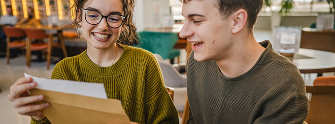 Two young adults hold and open envelope with letter read good news at cafe