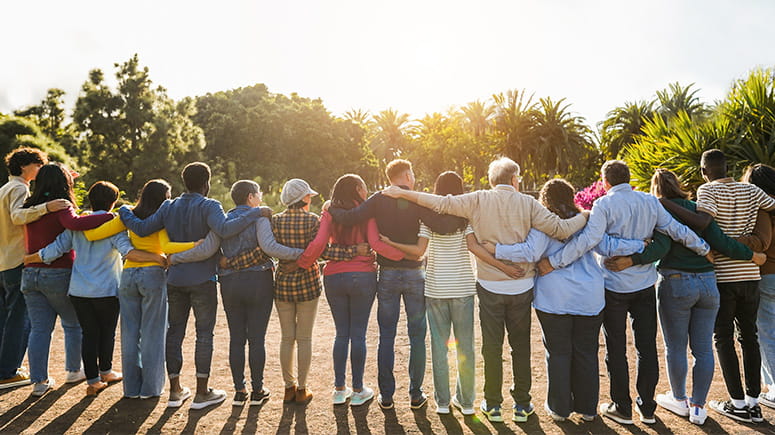 Group stands with arms around each other facing away from the camera towards the sunset.