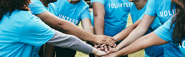 Volunteers in blue shirts that say "volunteer" put their hands together as a team
