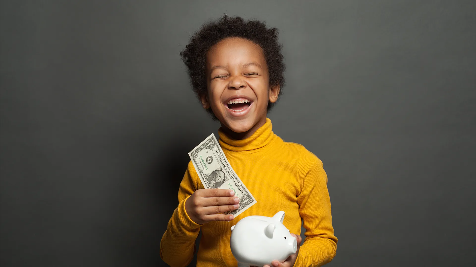 Child with yellow turtleneck puts a dollar into a piggy bank.