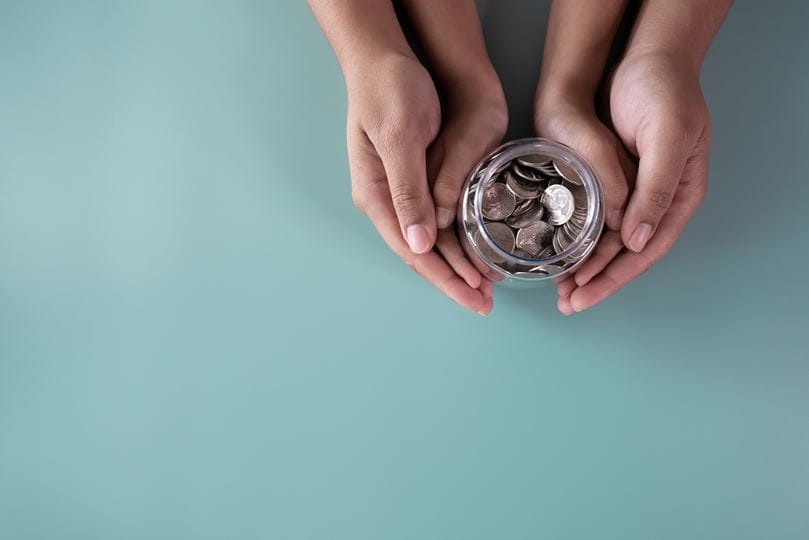 A parent and child hold a small jar of coins.