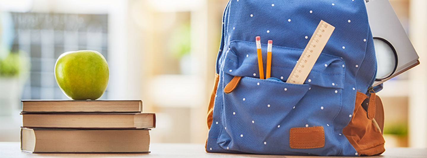Back back with school supplies, book and apple in classroom