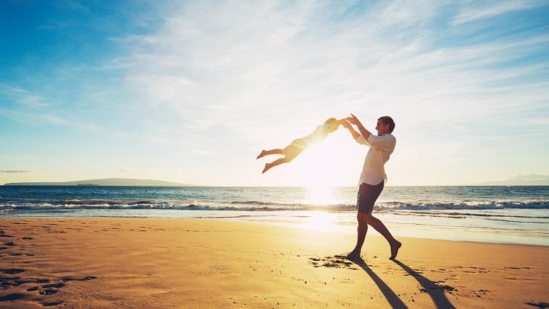 Man swinging son on beach at sunset