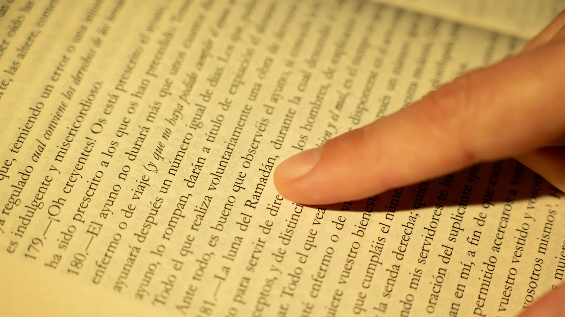 A closeup of a person pointing at text in Spanish in a book.