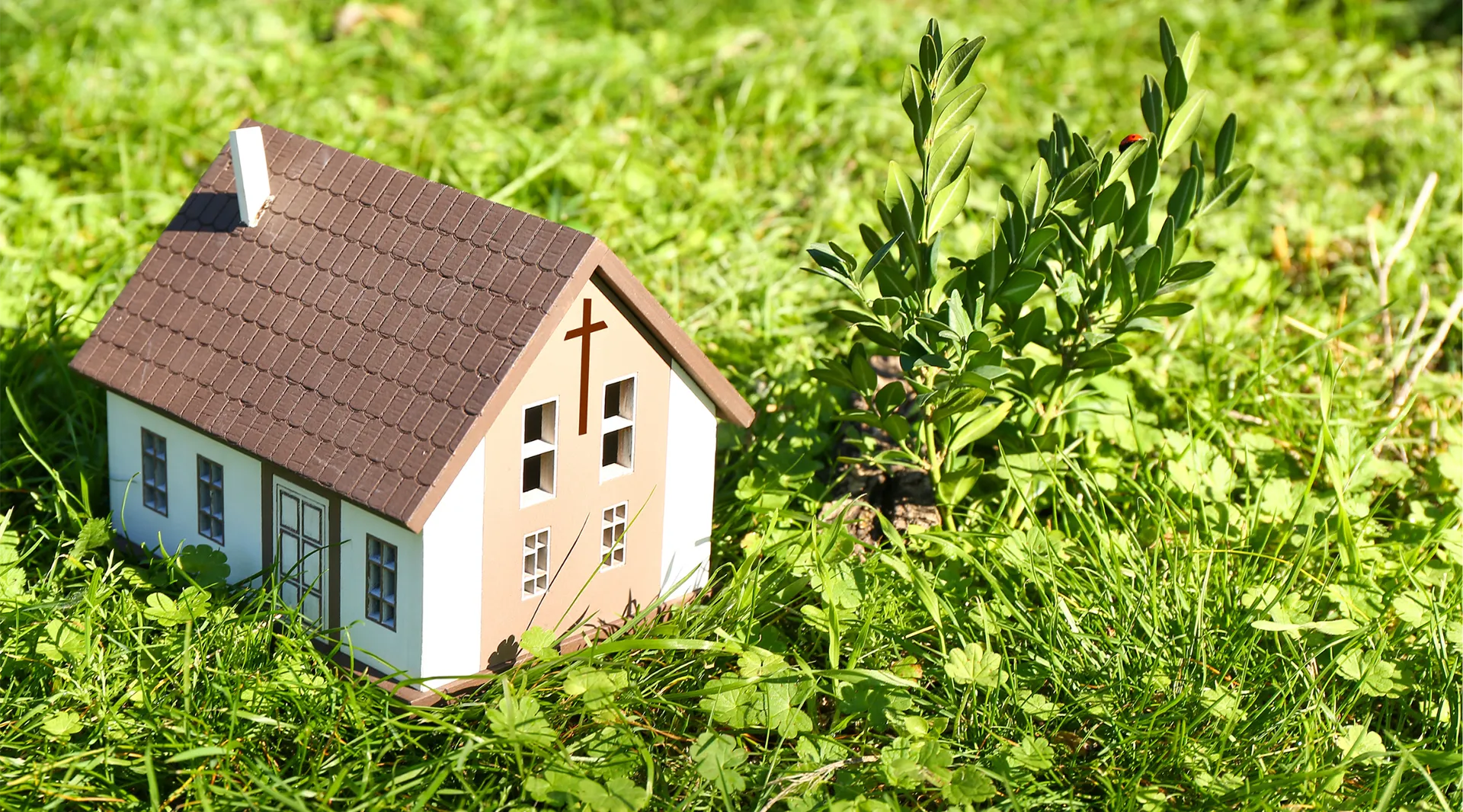 Small model church sitting in the grass.