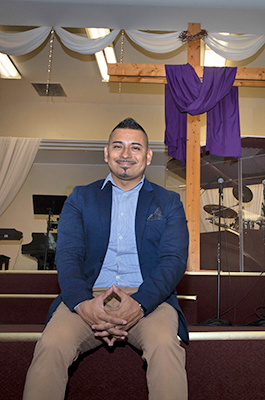 Sergio Nava from Sonido de Alabanza sits in old sanctuary with large wooden cross in background