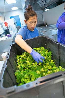 Woman scooping broccoli out of a bin.