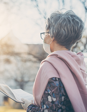 Woman with mask on reads a book outside