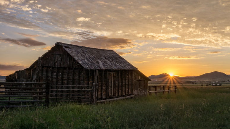 A barn at sunset. Mountains in the horizon.
