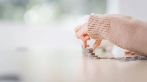 A small hand stacks coins on a surface