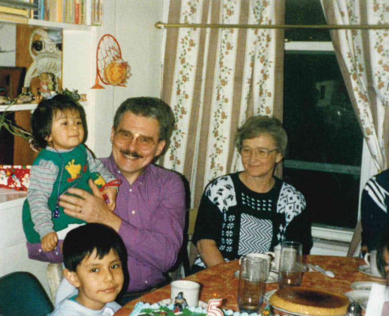 A man, woman, boy and girl sitting at a table. The man is holding the small girl while smiling at the camera