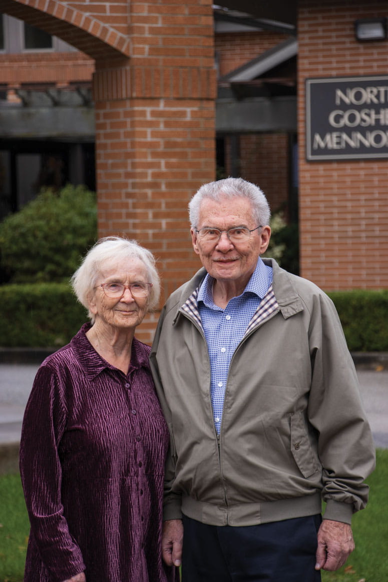 A man and a woman stand in front of a building, posing for a photo