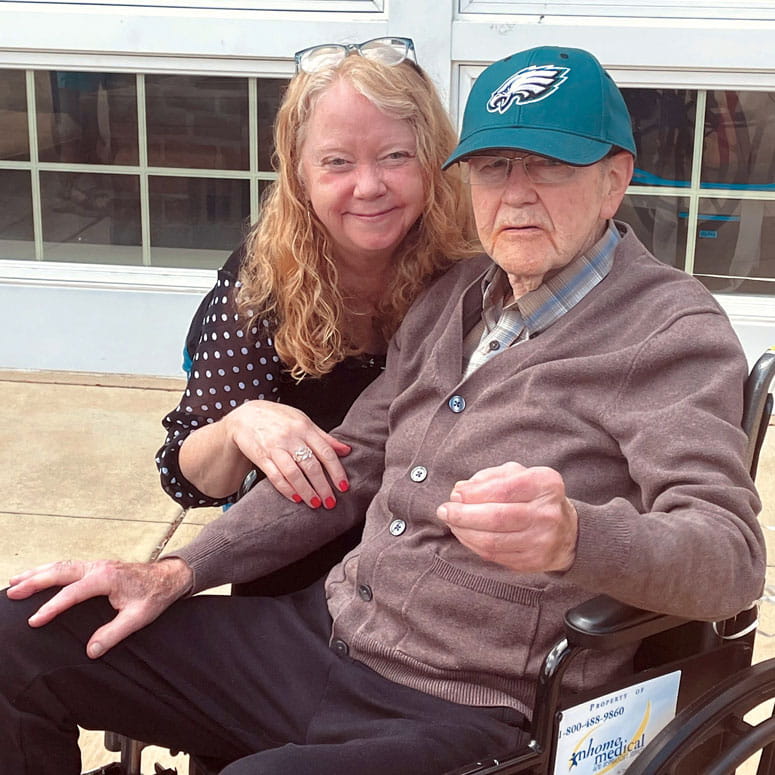 A woman poses with her father, who sits on a wheelchair 