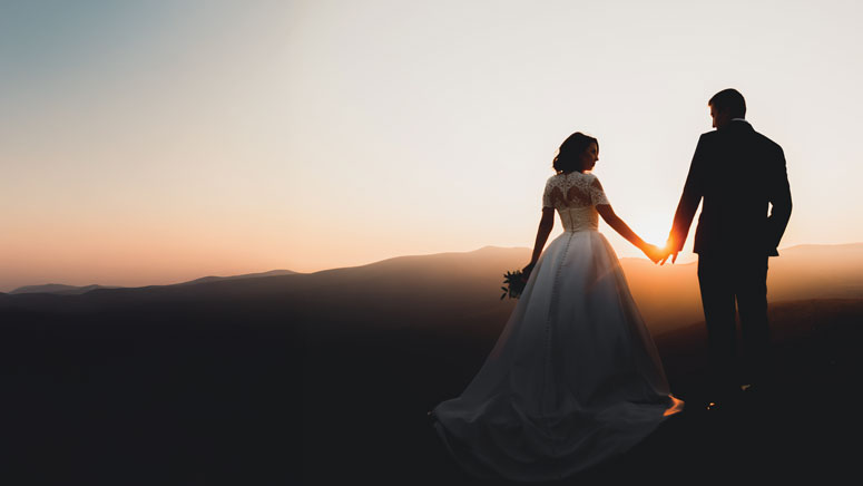 A newly wed husband and wife hold hands in the twilight