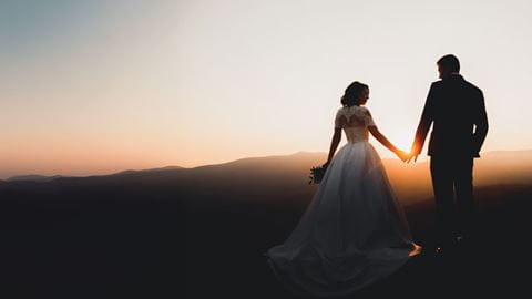 A newly wed husband and wife hold hands in the twilight