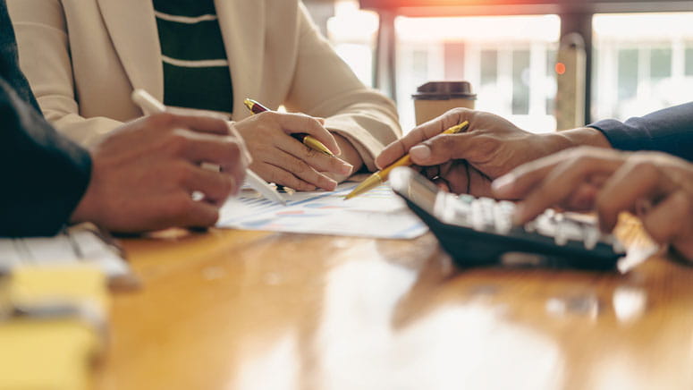 A close up on three people's hands as they write and use a calculator