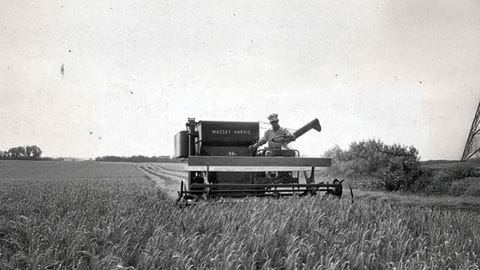 A farmer riding on farming equipment, working the field 