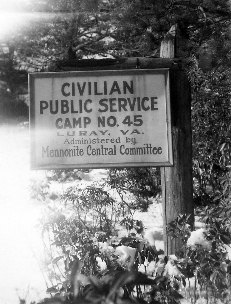 A black-and-white photo taken in the 1940s shows a sign for a civilian public service camp