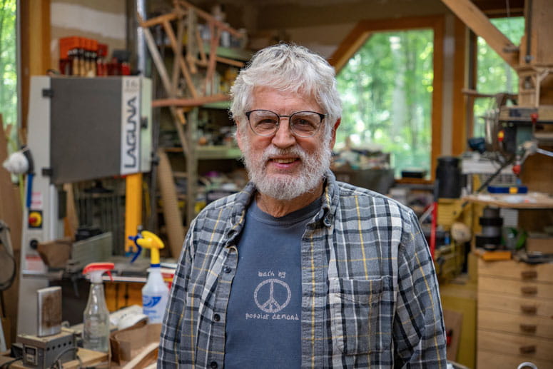 A man stands in his woodworking workshop, posing for a photo