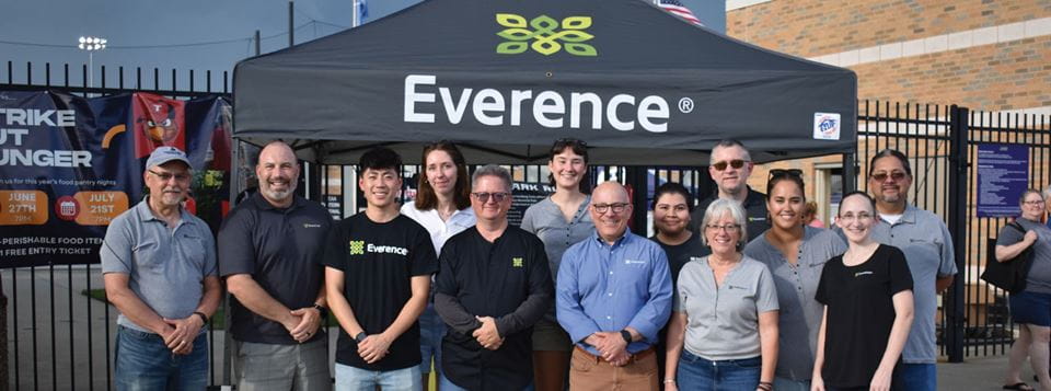 A large group of people stand posing for a photo outside a stadium, in front of a tent with "Everence" written on it