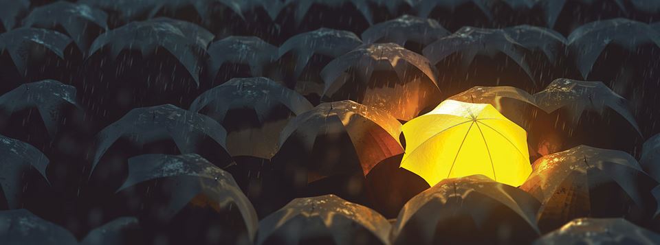 A glowing umbrella in a sea of black umbrellas