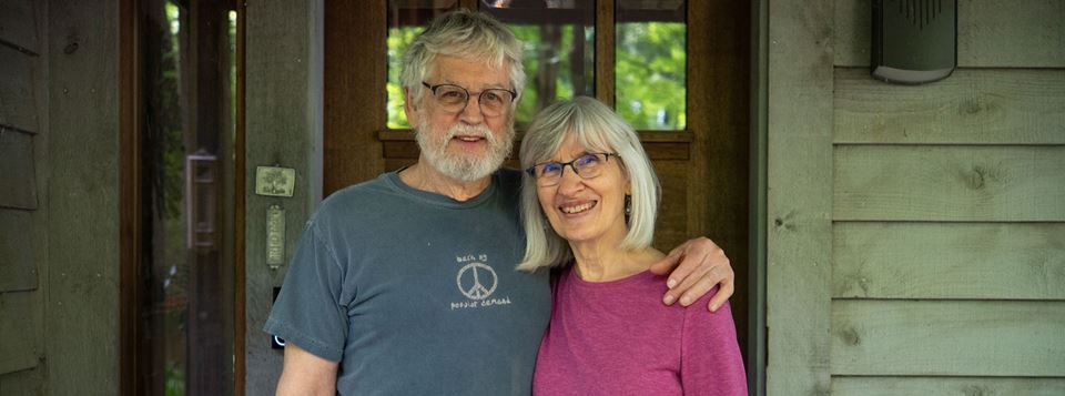 A couple, recently retired, poses for for a photo outside its home