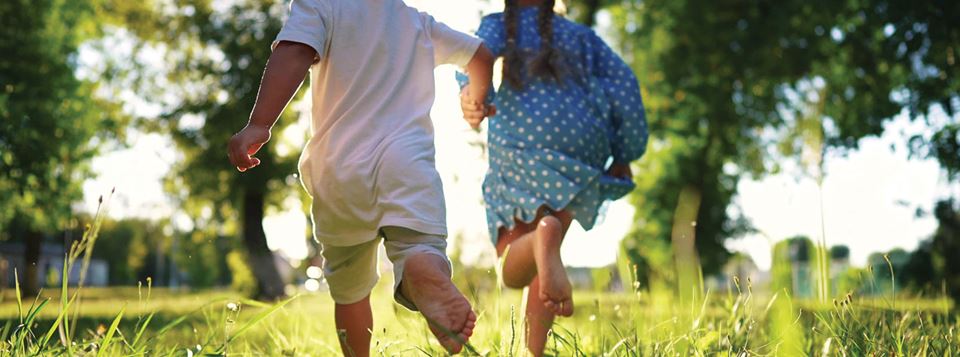 Kids holding hands running through fields with grass and trees in golden hour light.