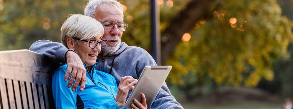 Couple sitting on a bench looking at a tablet together.