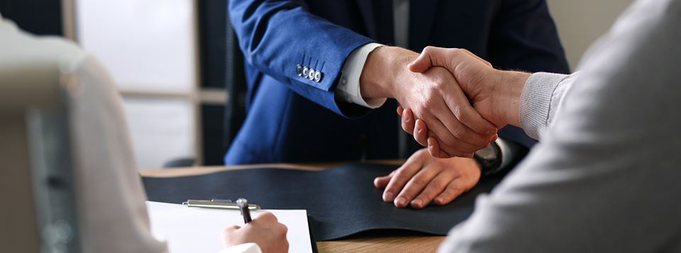 Professional man shaking hands with a couple across a table.