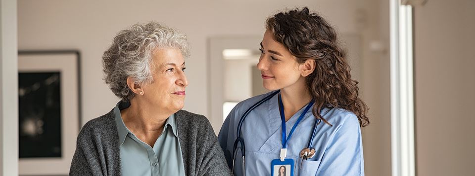Woman and nurse walking through nursing home arm in arm.
