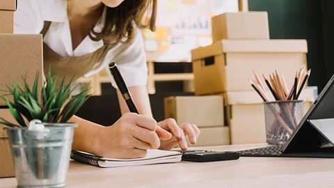 A woman takes notes at the counter while unpacking and setting up her small business.
