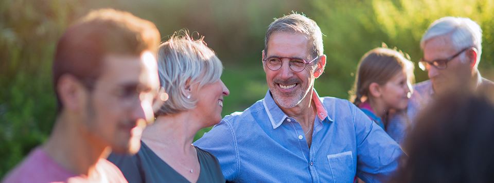 A man surrounded by his family outdoors smiles at his wife.