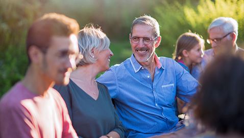 A man surrounded by his family outdoors smiles at his wife.