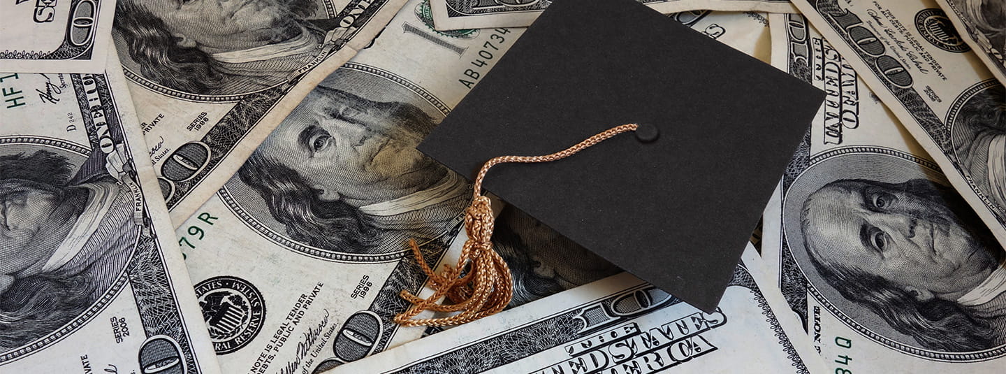 Grad cap sitting on top of hundred dollar bills