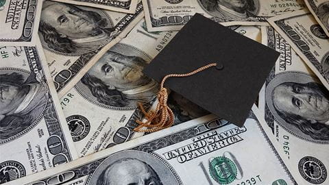 Grad cap sitting on top of hundred dollar bills