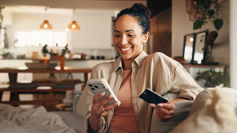 Woman using credit card on phone while sitting in a cozy house.