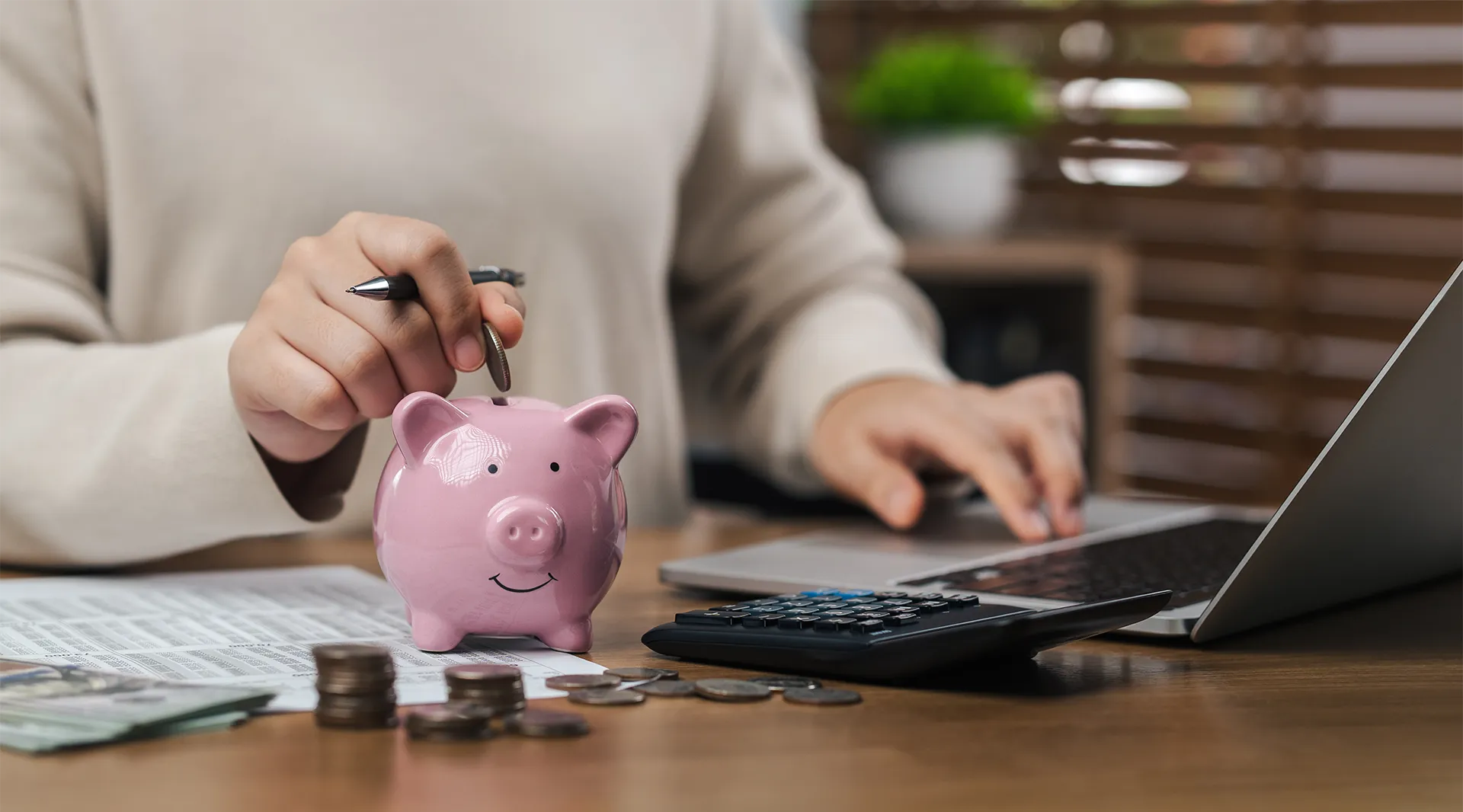 A person working on a laptop also puts a coin into their piggy bank.