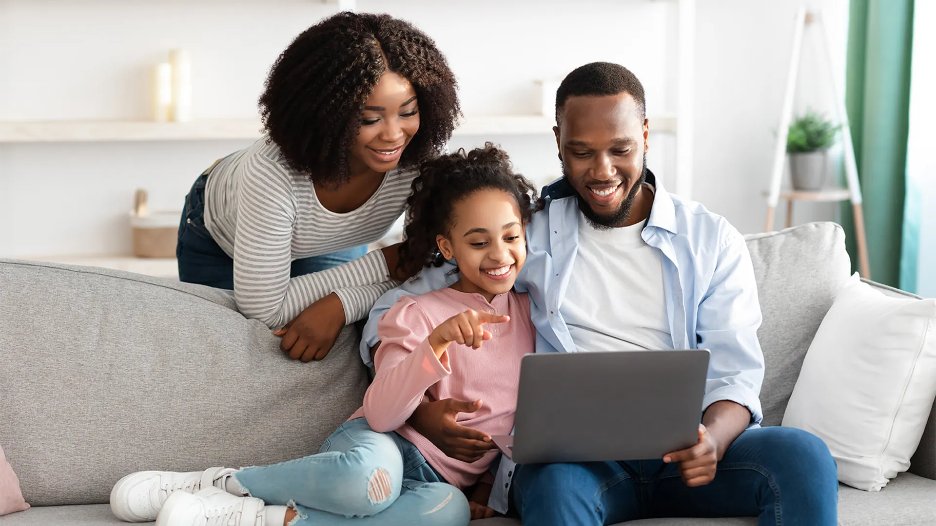 Black family of three sits on the couch happily looking at a computer together.