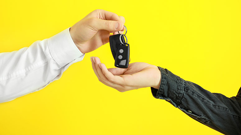 Two people exchanging vehicle keys, symbolizing a credit union auto refinance or planning with a motorcycle loan calculator.