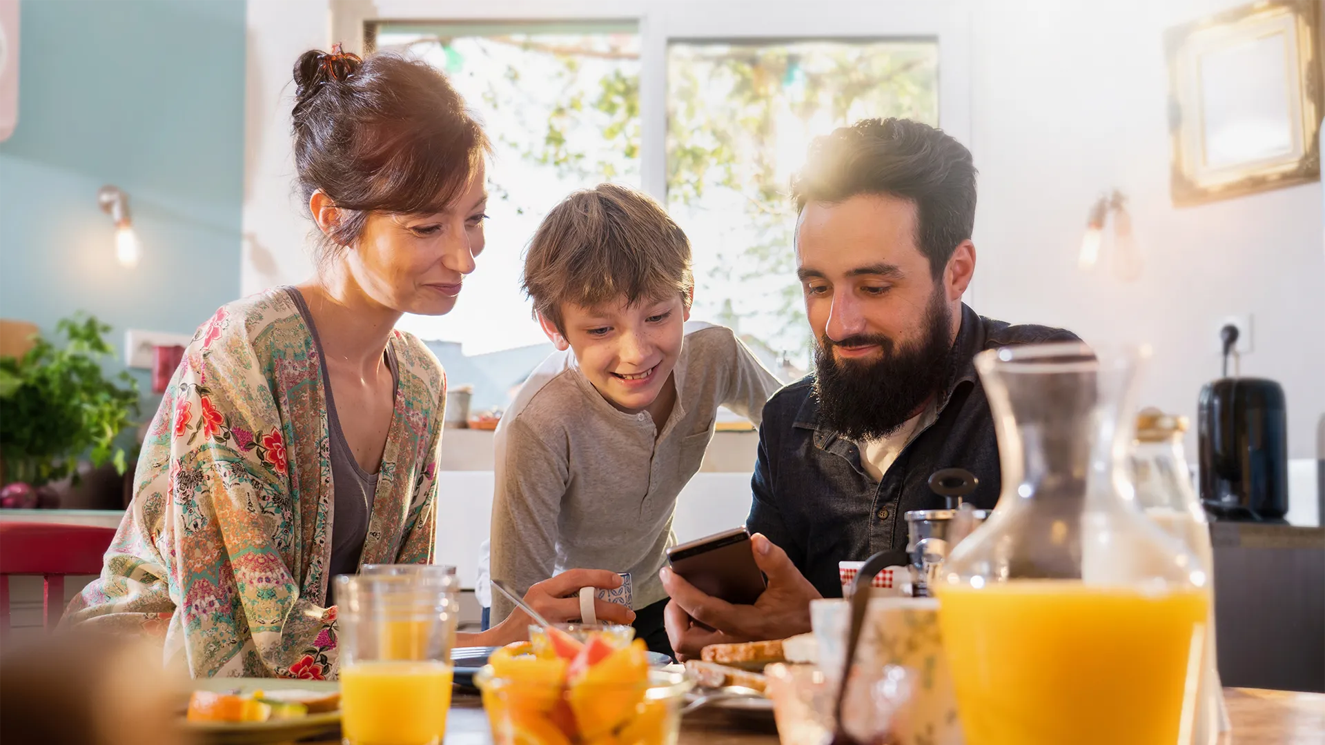 Family of three sitting in the kitchen looking at a phone.