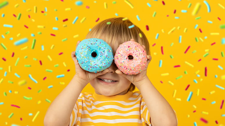 Young boy holds donuts up to his eyes with a confetti background