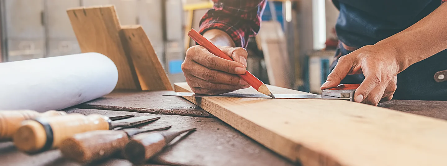 Carpenter uses a straight edge to draw a line across a wood board